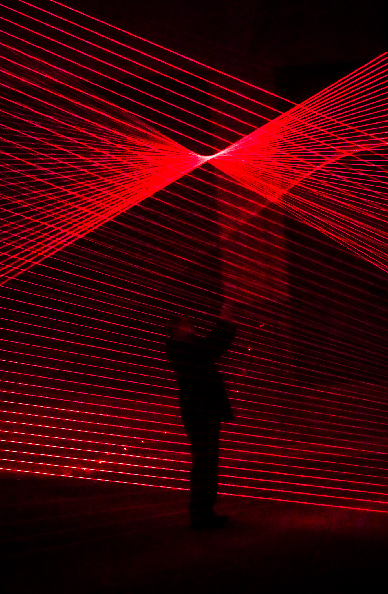 A silhouetted figure before a field of crossing red laser lines